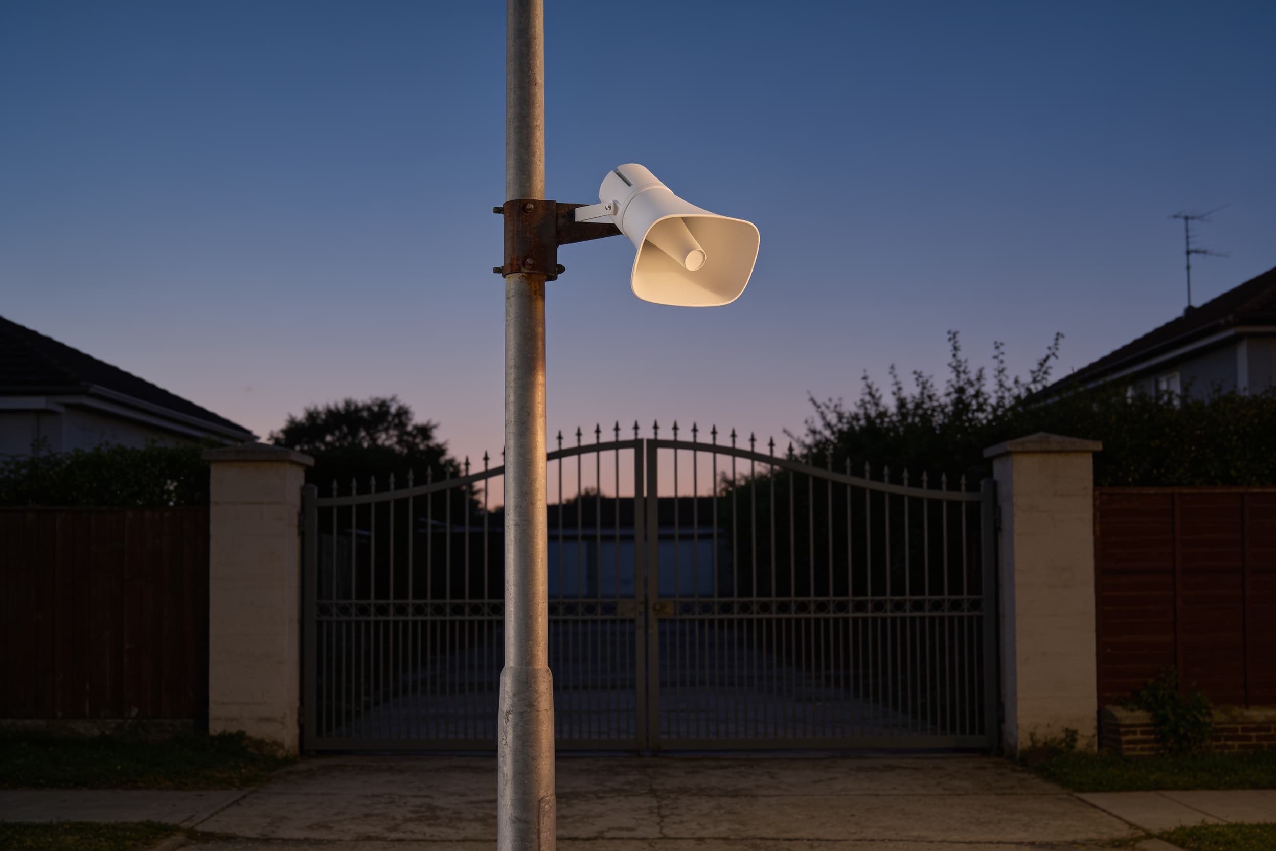 A loudspeaker on a pole above a gate at dusk