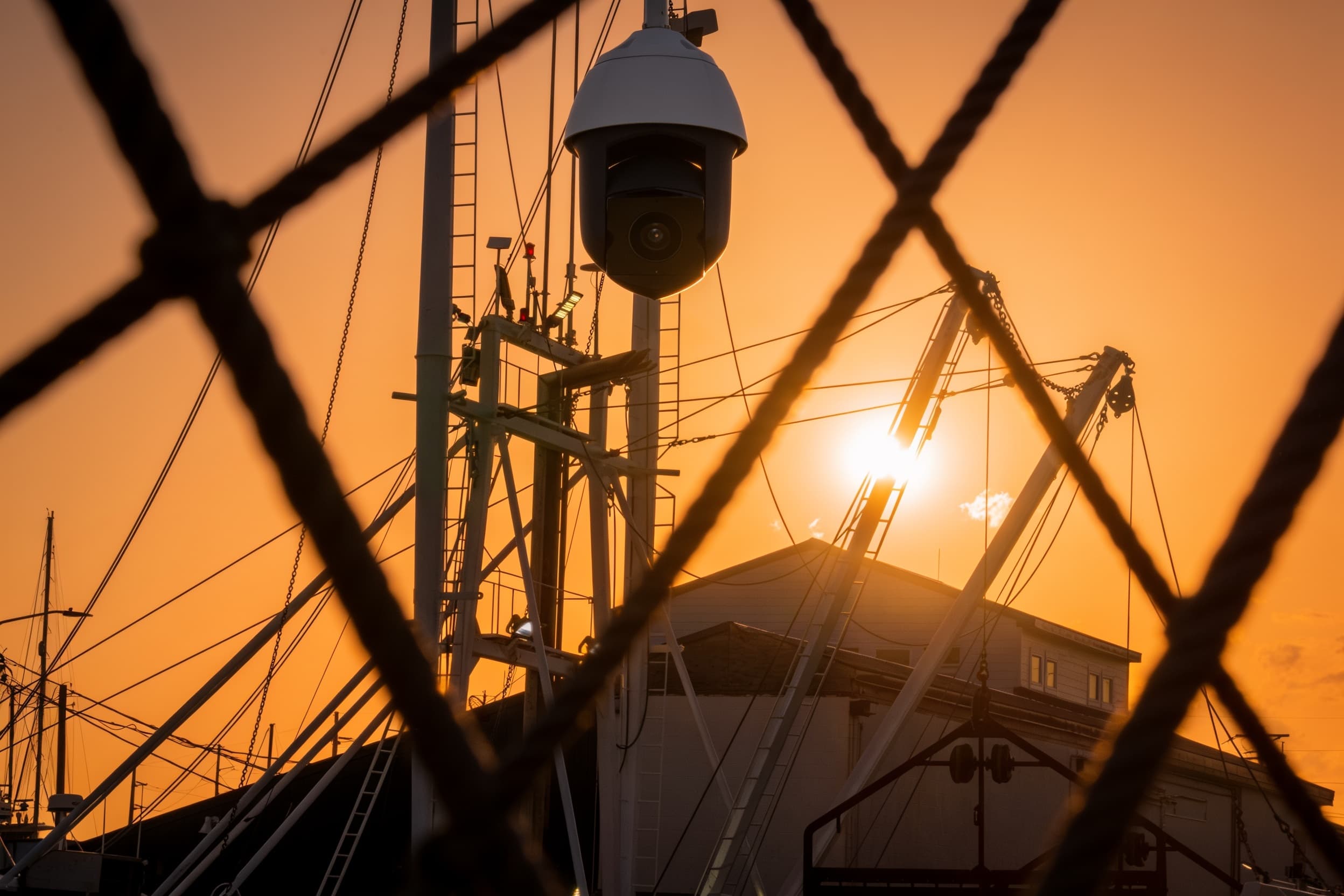 A security camera atop an industrial-yard mast at sunset
